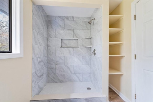 full bathroom featuring a wealth of natural light, tiled shower, and wood finished floors
