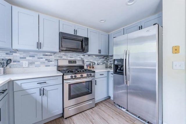 kitchen with stainless steel appliances, light wood-type flooring, light countertops, and backsplash