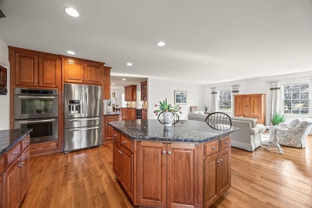 kitchen with appliances with stainless steel finishes, light hardwood / wood-style flooring, a kitchen island, and dark stone countertops