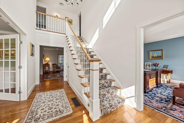 staircase with a notable chandelier, wood-type flooring, and a high ceiling