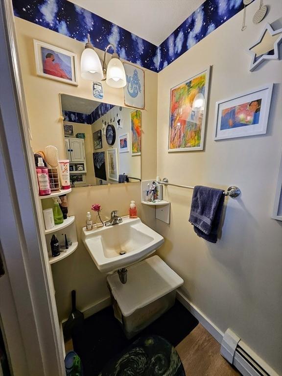 12 Sutton Ct Unit 12, Amherst, MA 01002 - bathroom with a baseboard radiator, a sink, wood finished floors, and baseboards
