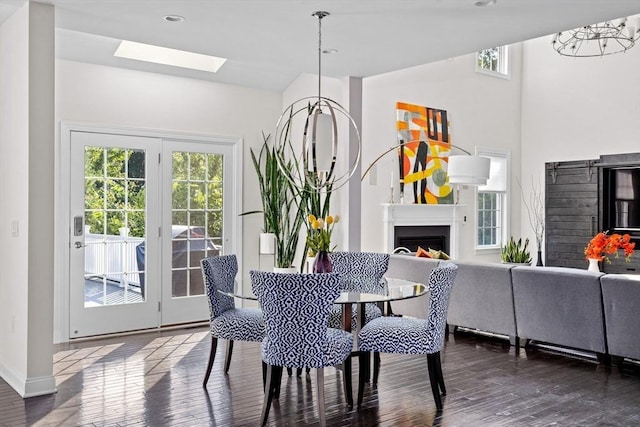 dining room featuring dark wood-style floors, a skylight, a notable chandelier, a fireplace, and baseboards