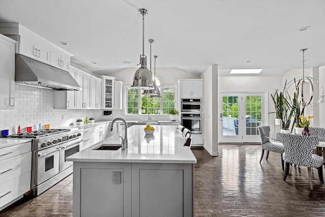 kitchen with stainless steel appliances, light countertops, a sink, an island with sink, and under cabinet range hood