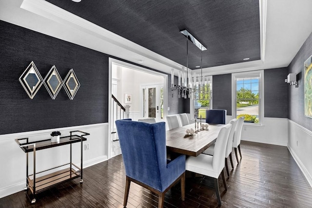 dining area with a wainscoted wall, dark wood finished floors, a raised ceiling, an accent wall, and wallpapered walls