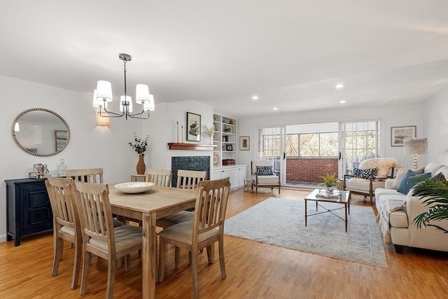 dining area with light wood-style floors, baseboards, recessed lighting, a tile fireplace, and a notable chandelier