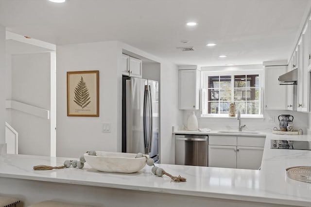kitchen with a sink, light stone counters, stainless steel appliances, and recessed lighting