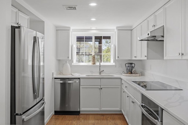 kitchen featuring a sink, light wood finished floors, stainless steel appliances, under cabinet range hood, and visible vents