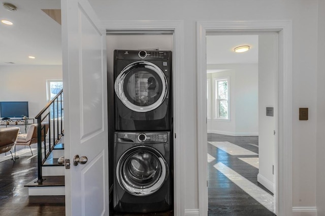 laundry room featuring stacked washer / drying machine, dark wood-type flooring, and a wealth of natural light