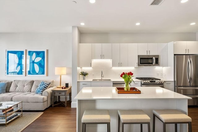 kitchen with dark wood finished floors, a sink, stainless steel appliances, a kitchen bar, and open floor plan