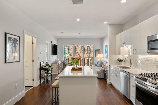 kitchen with modern cabinets, a breakfast bar, a sink, open floor plan, and appliances with stainless steel finishes