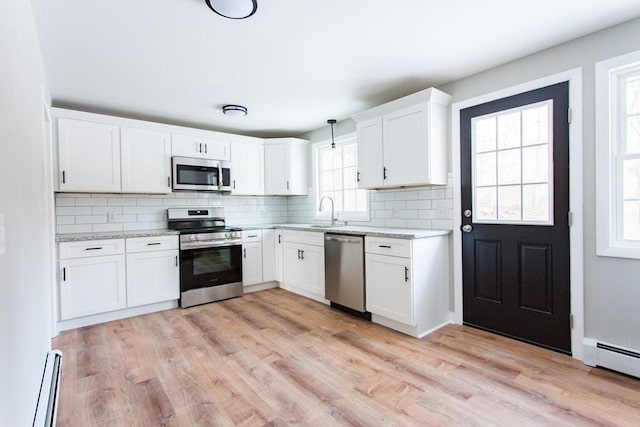 kitchen with appliances with stainless steel finishes, hanging light fixtures, white cabinets, and a baseboard heating unit