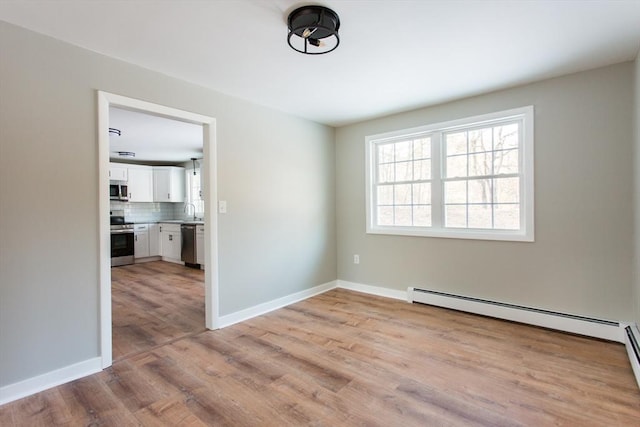 empty room featuring light hardwood / wood-style floors, a baseboard radiator, and sink