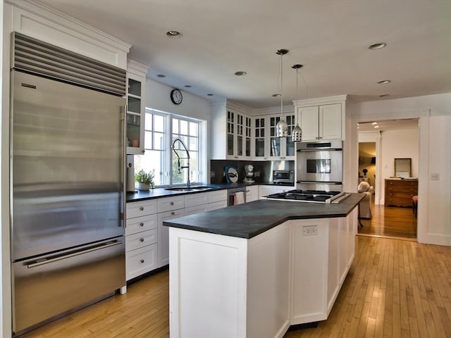 kitchen with white cabinets, dark countertops, appliances with stainless steel finishes, glass insert cabinets, and hanging light fixtures