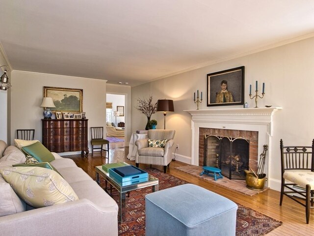 living room with a brick fireplace, ornamental molding, and wood finished floors