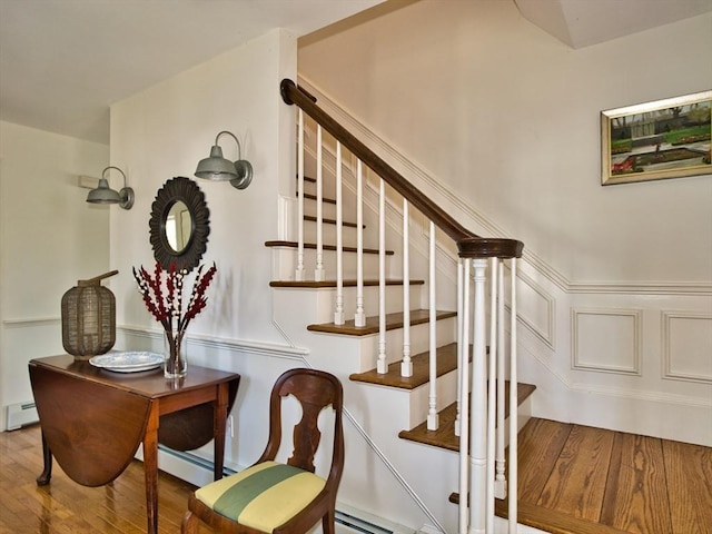 stairway featuring a baseboard heating unit, a decorative wall, and wood finished floors