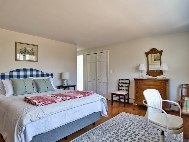 bedroom with a baseboard heating unit, a closet, and wood finished floors