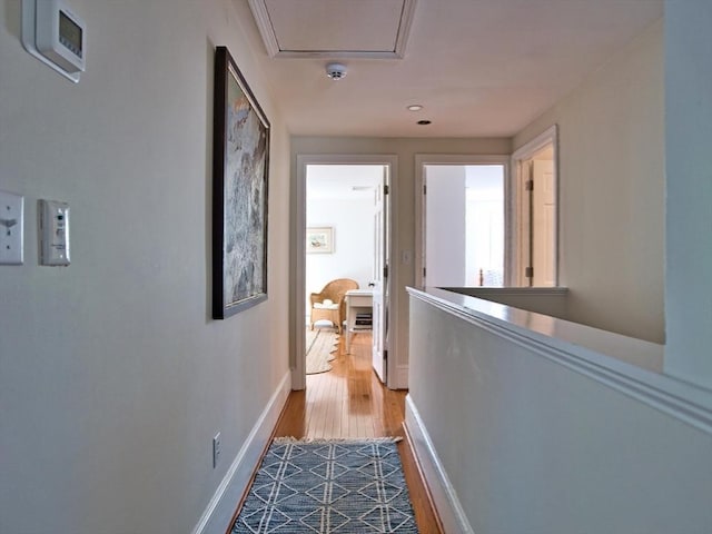 corridor with light wood-style floors, baseboards, and an upstairs landing