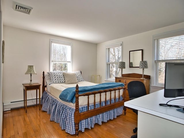 bedroom featuring a baseboard heating unit, multiple windows, visible vents, and light wood-style floors