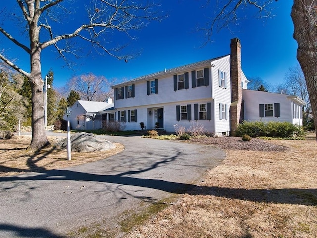 colonial inspired home with a chimney and aphalt driveway