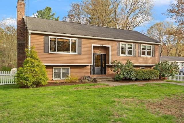 split foyer home with fence, a chimney, and a front lawn