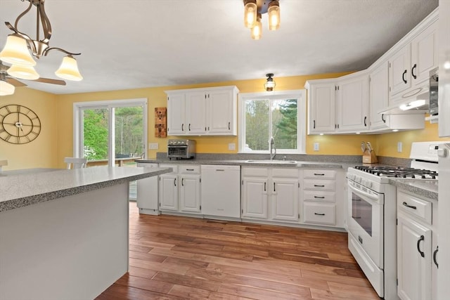 kitchen with white cabinets, a sink, light wood finished floors, white appliances, and light countertops