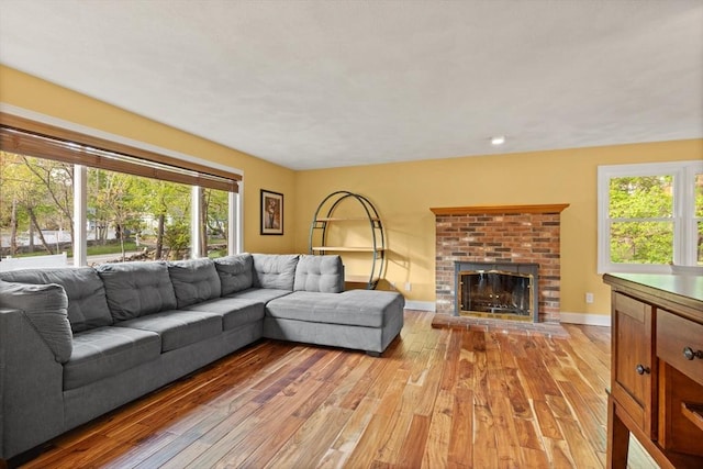living room featuring baseboards, a brick fireplace, and light wood-type flooring