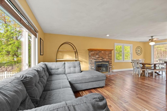 living area featuring baseboards, a ceiling fan, wood finished floors, and a fireplace