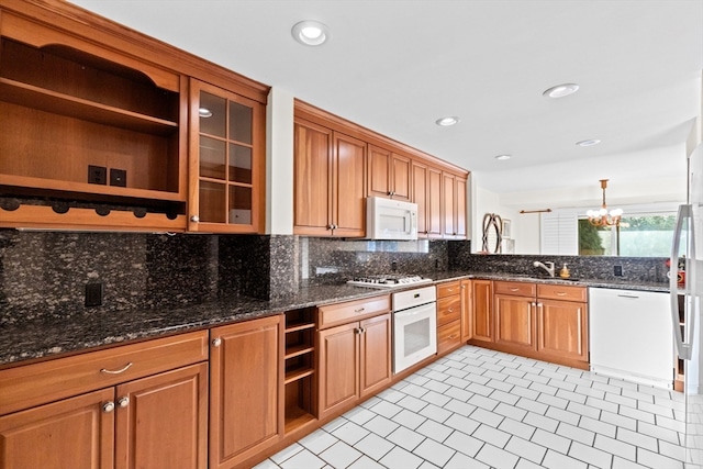 kitchen with dark stone counters, white appliances, a chandelier, and hanging light fixtures