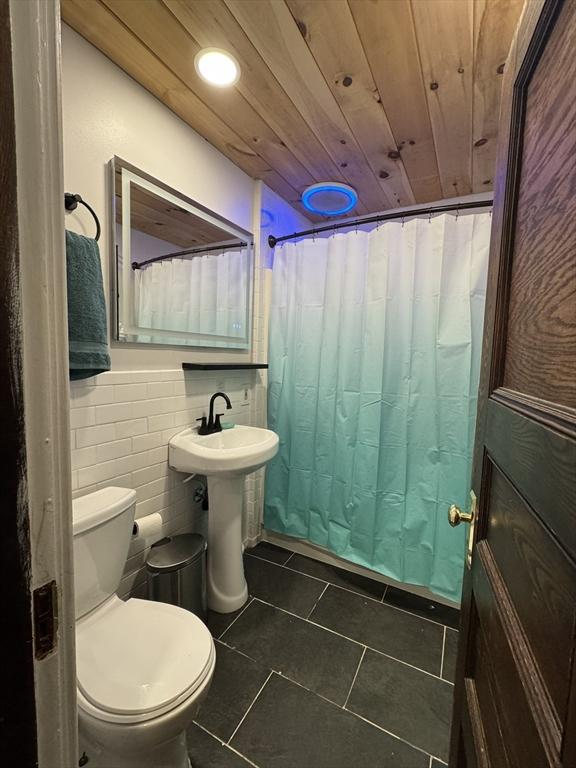 bathroom featuring toilet, wood ceiling, tile walls, a shower with curtain, and sink