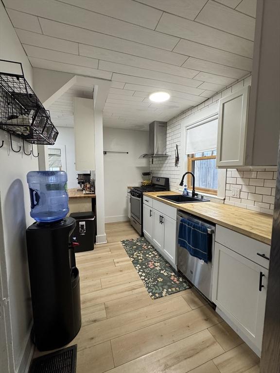 kitchen featuring butcher block counters, wall chimney exhaust hood, stainless steel range with gas cooktop, and dishwashing machine