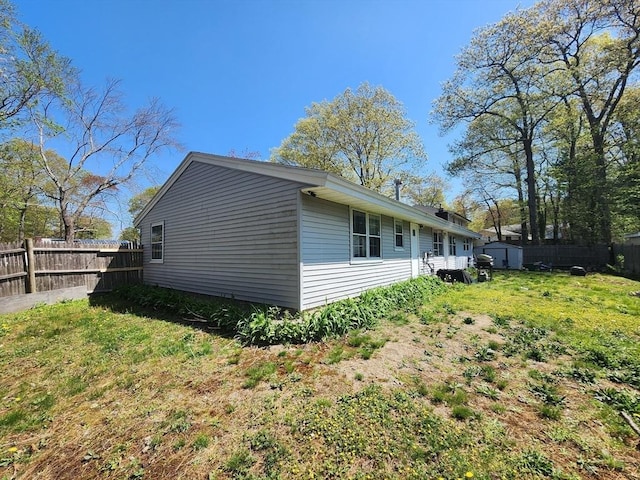 view of side of property with a yard, an outdoor structure, a fenced backyard, and a storage unit