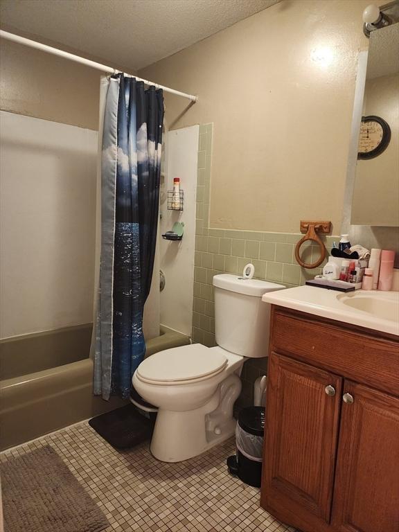 full bathroom with tile walls, toilet, wainscoting, vanity, and shower / bath combo