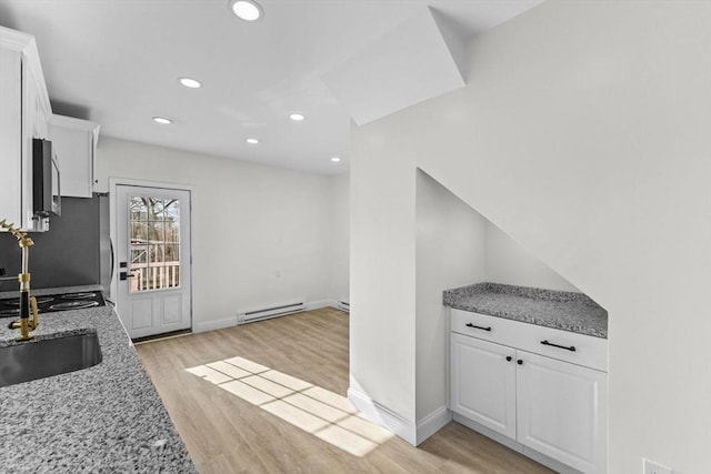 kitchen featuring a baseboard heating unit, white cabinetry, light wood-type flooring, stainless steel appliances, and light stone counters