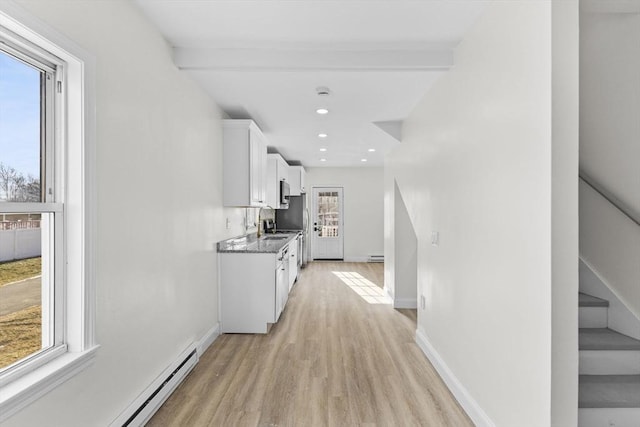 kitchen with a baseboard radiator, white cabinets, dark stone counters, beam ceiling, and light hardwood / wood-style flooring