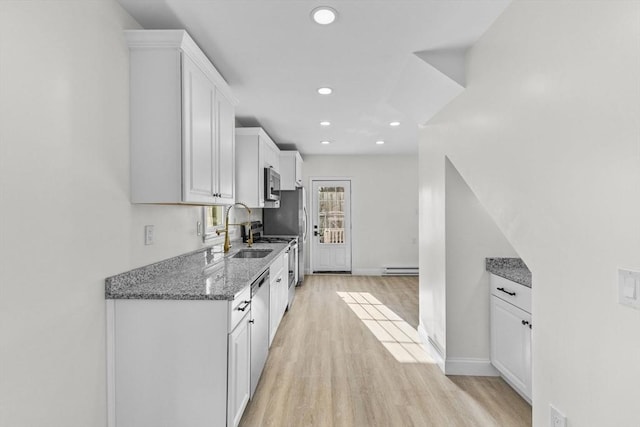 kitchen featuring white cabinetry, appliances with stainless steel finishes, dark stone countertops, light hardwood / wood-style flooring, and sink