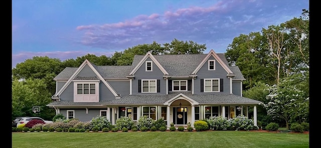 shingle-style home featuring covered porch and a front yard