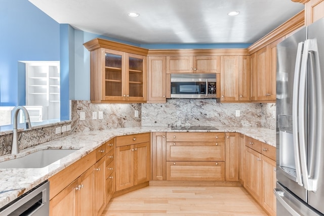 kitchen with sink, stainless steel appliances, light stone counters, light hardwood / wood-style flooring, and decorative backsplash