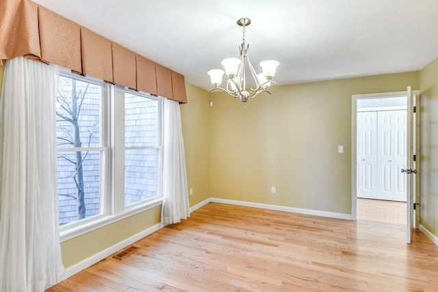 unfurnished room featuring a notable chandelier and light hardwood / wood-style flooring