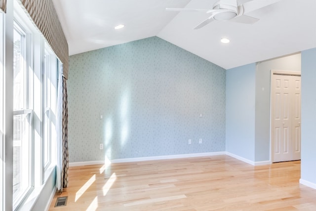 empty room featuring a wealth of natural light, ceiling fan, lofted ceiling, and light wood-type flooring