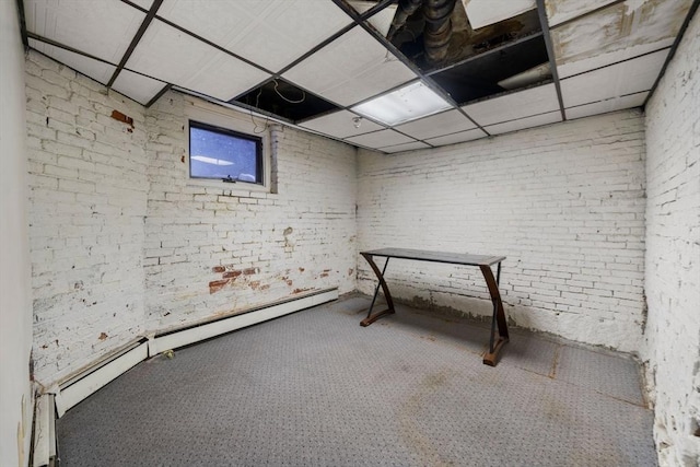 basement featuring baseboard heating, brick wall, and a drop ceiling