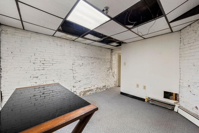 basement featuring a paneled ceiling, brick wall, and baseboard heating