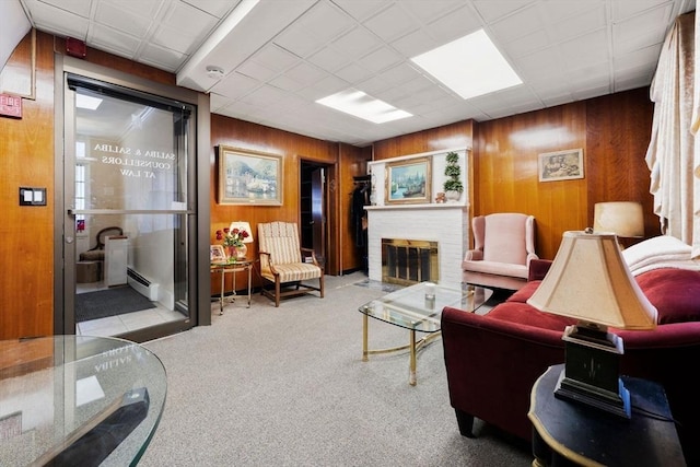 carpeted living room featuring a brick fireplace, wood walls, and baseboard heating