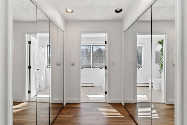 hallway with a baseboard radiator, baseboards, and wood finished floors