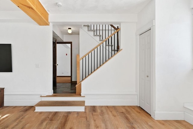 stairway with beamed ceiling, wood finished floors, and baseboards