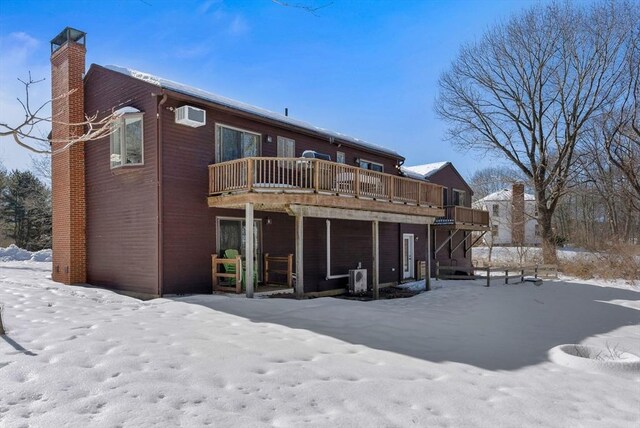 snow covered house with an AC wall unit, a chimney, and a wooden deck