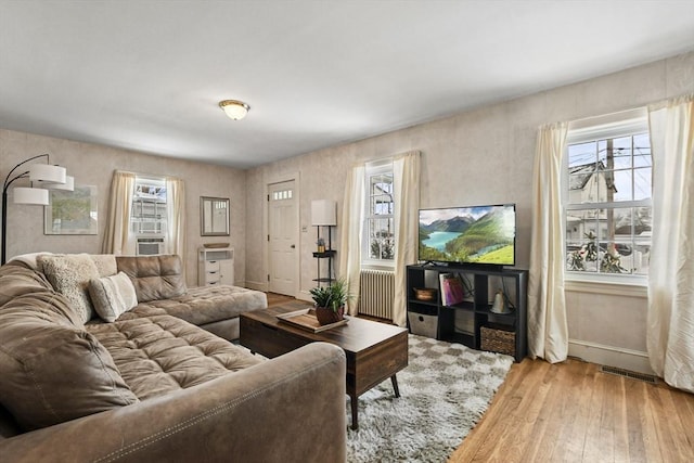 living room featuring wood-type flooring, radiator heating unit, cooling unit, and a healthy amount of sunlight