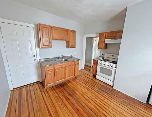 kitchen featuring baseboards, a sink, light wood-style floors, under cabinet range hood, and white gas stove