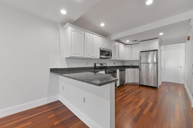 kitchen with kitchen peninsula, dark wood-type flooring, stainless steel appliances, decorative backsplash, and white cabinetry