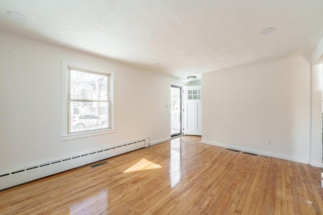 spare room featuring light wood-type flooring, a baseboard radiator, a wealth of natural light, and baseboards