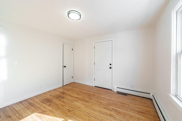 unfurnished room with a baseboard heating unit, baseboards, and light wood-style floors